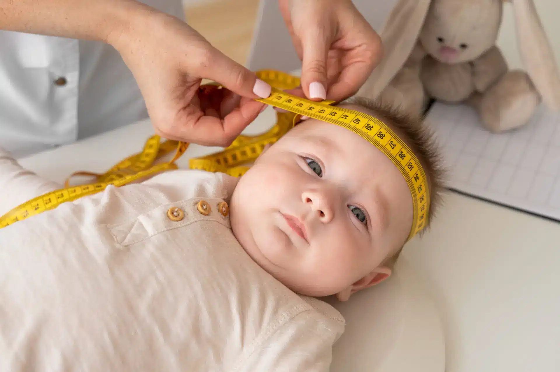 Bebê em consulta pediátrica com profissional medindo o perímetro cefálico, acompanhando crescimento e desenvolvimento saudável
